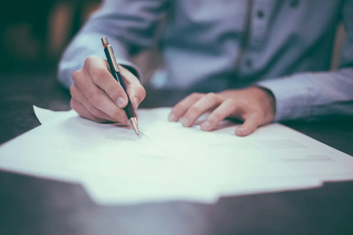 Persona firmando un contrato con documentación sobre la mesa